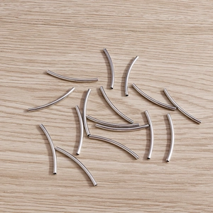 Perles tubes courbées en métal poli pour la création de bijoux DIY sur fond de bois clair