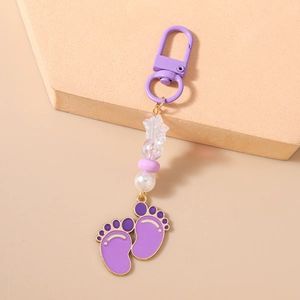 Detail of purple paw pendant keychain with star beads and metallic charms on beige surface
