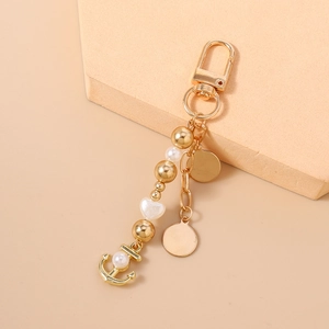 Détail du porte-clés perles dorées avec pendentif ancre et plaques en métal sur bloc beige