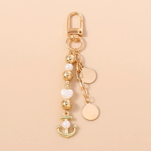 Détail d'un porte-clés ancre doré avec perles et breloques en métal sur fond beige