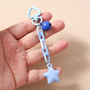 Hand holding a blue star keychain with a heart clasp and metal bell on a beige background