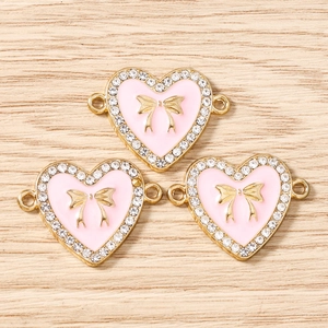 Detailansicht der rosa Emaille-Herzanhänger mit goldenen Schleifen und funkelnden Strass