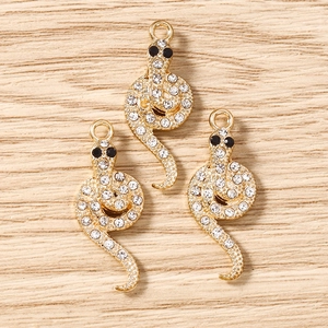 Vue détaillée de trois pendentifs serpent dorés sertis de strass sur fond en bois clair