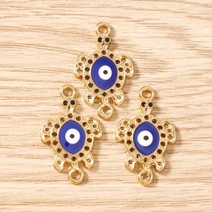 Macro detail of three golden sea turtle evil eye pendants on light wood background