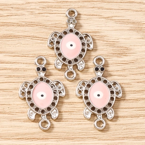Detailed view of silver turtle charms with pink enamel and evil eye for DIY jewelry making