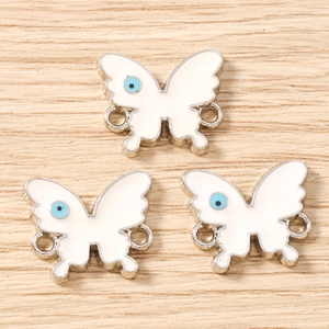 Three white enamel butterfly charms with blue dots and silver double rings on wood
