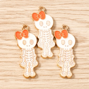 Detailed view of three skull charms with orange bows and gold-plated enamel finish