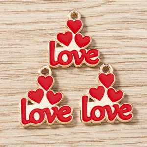 Macro detail of three golden heart charms with red enamel and Love lettering