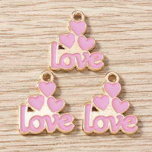 Macro shot of three pink enamel heart pendants with LOVE letters and metal hanging loops