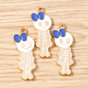 Three gold skull charms with blue bows and white enamel on a light wood surface