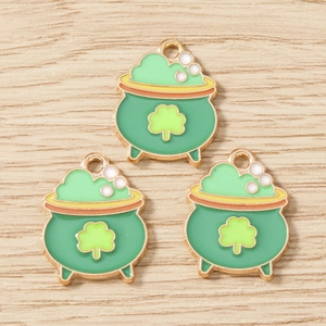 Three St. Patrick's Day green pot charms with gold clover detailing on wooden surface