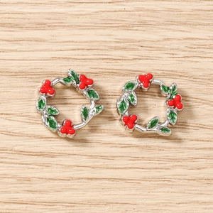 Detail view of festive green and red enamel holly wreath charms on a wooden surface
