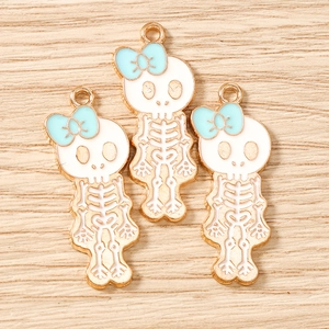 Detail of three cartoon skull enamel charms with blue bows on a light wood background