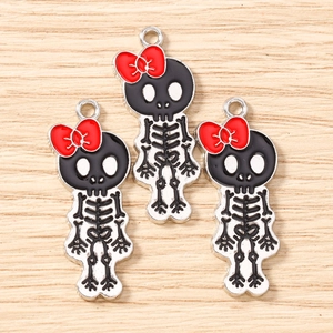 Three skeleton pendants with red bows and black enamel details on a light wood background