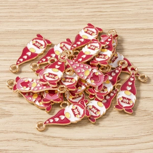 Close-up of red enamel Christmas gnome charms with golden loops on light wood background
