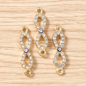 Detail von goldenen Unendlichkeit-Anhängern mit Evil-Eye-Perle und Strass-Verzierung