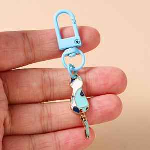 Detail of blue cat pendant keychain with spring hook held in hand against warm background