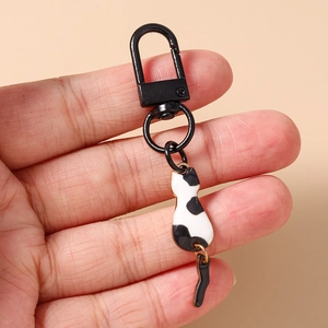 Cute black and white cat keychain with a movable tail held in hand for scale