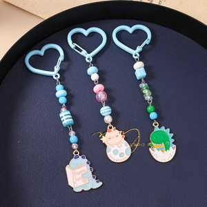 Porte-clés dinosaures colorés avec perles pastel et pendentifs émaillés dans un plateau bleu