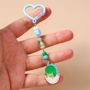 Détail d'un porte-clés dinosaure avec fermoir cœur bleu et perles dégradées colorées
