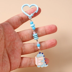 Détail d'un porte-clés dinosaure bleu avec des perles et un crochet en forme de cœur
