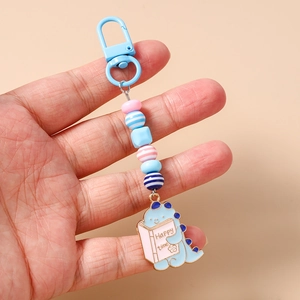 Detail of cute blue cartoon dinosaur keychain with colorful beads held in hand