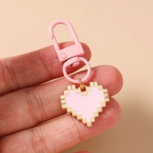Detailed view of pink pixel heart keychain with gold edges held in hand on solid background