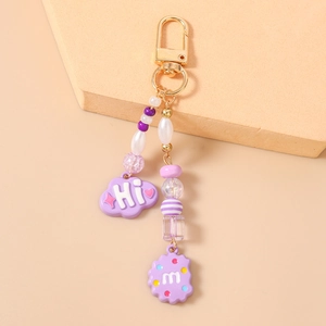 Close-up of purple beaded keychain featuring cloud and cookie charms with gold D-ring