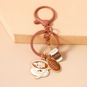 Detail of coffee-themed keychain with latte cup and coffee bean charms on a beige surface