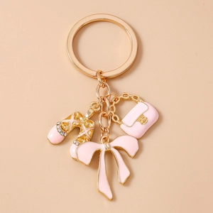 Detailed view of pink enamel ballet shoe, handbag and bow charms on a gold keychain
