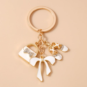Detailed close-up of golden keychain with white enamel ballet shoes and rhinestone bow charms