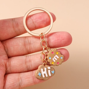 Close-up of cartoon cookie and cloud pendants on a golden metal keychain with Hi and m letterings