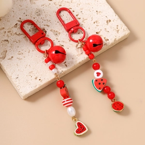 Handmade red beaded watermelon keychains with bells and heart charms on a stone background
