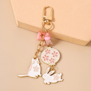 Detailed view of enamel cat and rabbit charms with cherry blossom patterns on gold keychain
