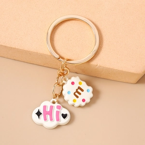 Close-up of golden keychain with cloud pendant and cookie charm on beige background