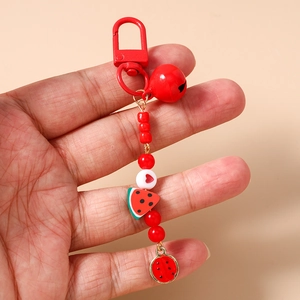 Close-up of watermelon beaded keychain with red bell and heart charm held by hand