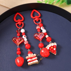 Close-up of strawberry cake charms with red heart clasps on a textured navy tray