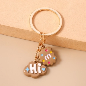 Detail of golden keychain with cartoon cookie 'm' and cloud 'Hi' charms on stand