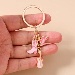 Macro shot of pink cowboy boot, hat, and guitar enamel charms on a gold keychain