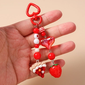 Detail of red heart keychain featuring beaded elements with strawberry cake and berry charms