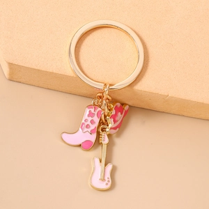 Close-up of pink enamel cowboy boot, guitar and hat charms on a golden keychain ring