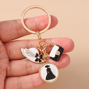 Détail du porte-clés doré avec charms chapeau émaillé, sac à main et silhouette féminine ronde