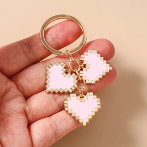 Detail of pixel heart keychain with gold ring and pink enamel charms in hand