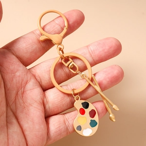 Detailansicht eines goldenen Künstler-Paletten-Schlüsselanhängers mit Pinseln in der Hand