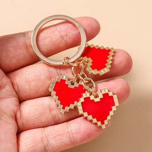 Detail of red pixel heart keychain with gold ring held in hand on warm background