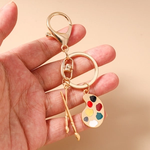 Detailansicht eines goldenen Künstlerpaletten-Schlüsselanhängers mit Pinseln in der Hand