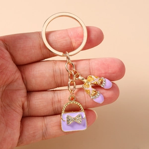 Detailed close-up of a golden keychain featuring purple enamel ballet shoes and a handbag
