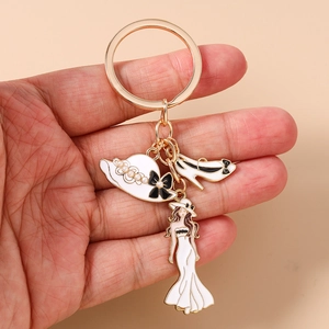 Détail du porte-clés doré avec charms en émail blanc chapeau, talon haut et silhouette dame