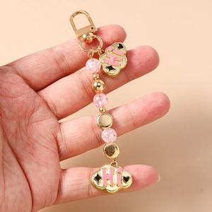 Close-up of pink beaded keychain with gold cloud pendants and HI lettering on beige background