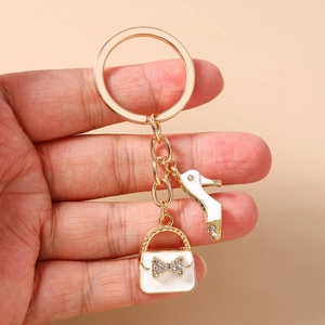 Detail of gold keychain with white enamel high heel and rhinestone bow handbag charm